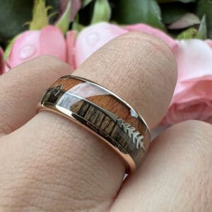 A ring finger wears the Kyler to showcase its dual wood inlay, gold-plated edge and sleeve, arrow design, and polished finish.