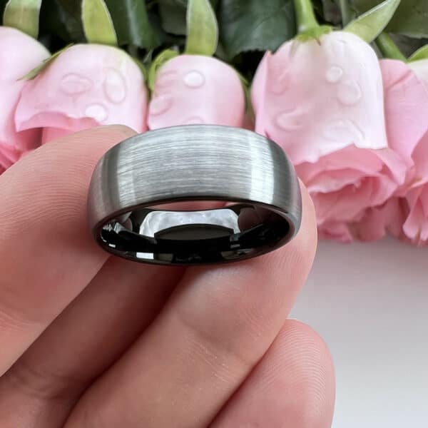 Modern gray men's wedding band featuring a brushed finish and a smooth and shiny black sleeve, resting on three fingers.