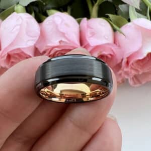 A simple contemporary wedding band featuring contrasting black brushed center and polished edges, and an 18K gold-plated polished sleeve, resting on three fingertips.