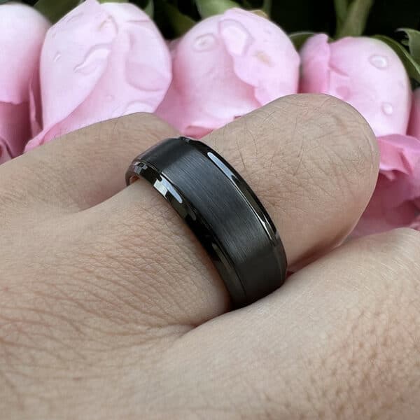 An 8mm bold modern men's wedding ring with a black elevated brushed center and polished edges on a ring finger.