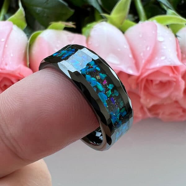 One finger holds a 8mm crystal wedding ring with blue and green opal inlays, carved beveled design edges, and polished finish.
