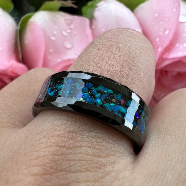 A ring finger wears The Tyson and exhibits its carved beveled design edge, blue and green opal inlays, and polished finish.