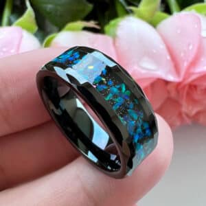 The Tyson, with its carved beveled design edges, blue and green crystal opal inlays, and black sleeve rests on three fingers.