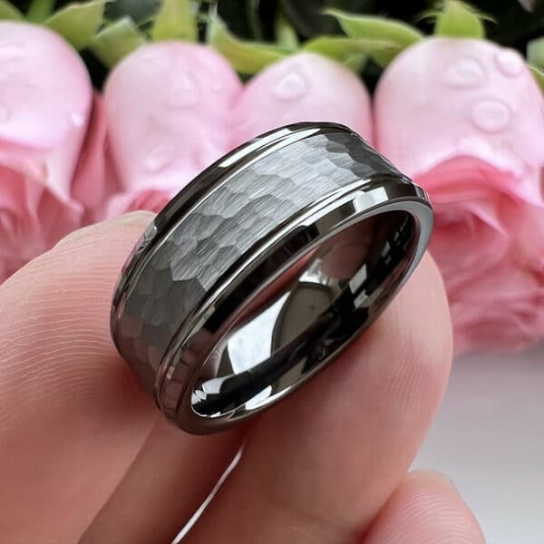 A 8mm tungsten men's wedding ring stands on three fingers to show its polished beveled edges and gunmetal hammered finish.