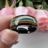 Two fingers help The Kevin to exhibit its black sleeve and edges, polished finish, blue opal center, and whiskey wood sides.