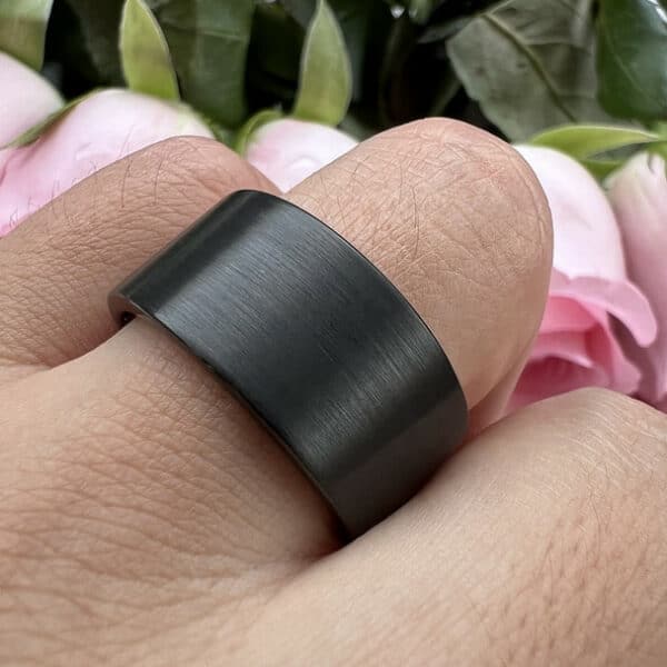 A ring finger wears The Aiden to showcase its unique black brushed finish, large size, and pipe-cut edges.