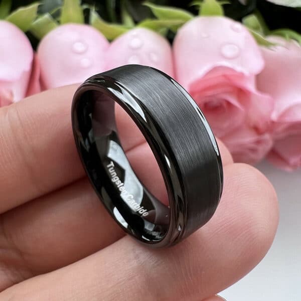 Three fingers support a black 8mm tungsten men's wedding band to showcase its polished edges, smooth sleeve, and brushed finish.