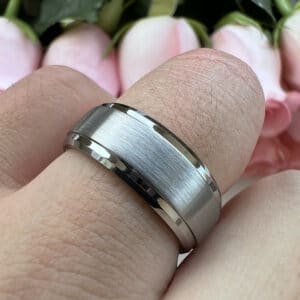 A ring finger poses with a silver-toned tungsten wedding band to showcase its brushed center and polished and beveled edges.