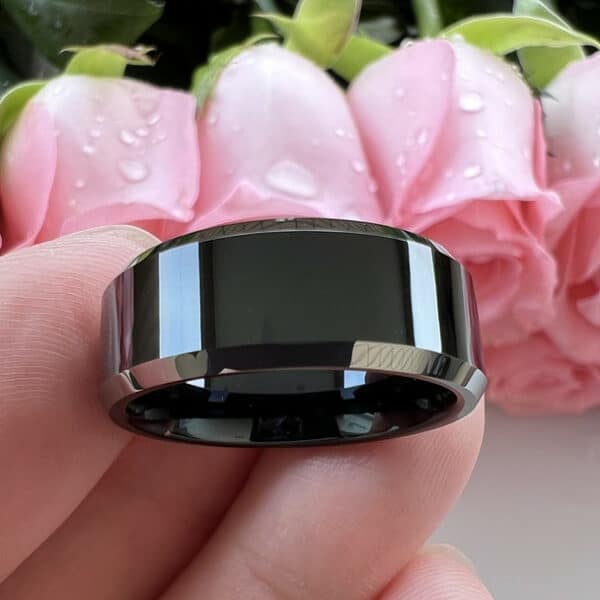 A unique 8mm black tungsten men's wedding band with silver edges and polished finish rests on three fingers.