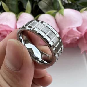 Three fingers hold a modern and industrial-themed wedding ring for men featuring a brushed center, polished edges, and a matrix design.