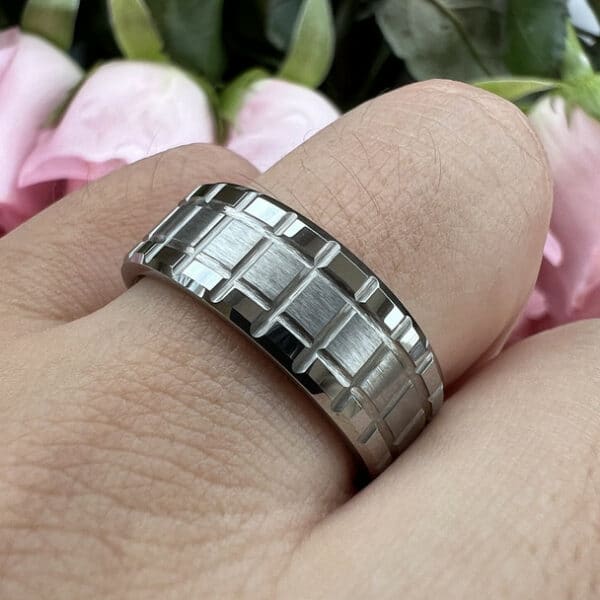A ring finger wearing a modern 8mm men's wedding ring that features a brushed center and polished edges that bear a matrix design.