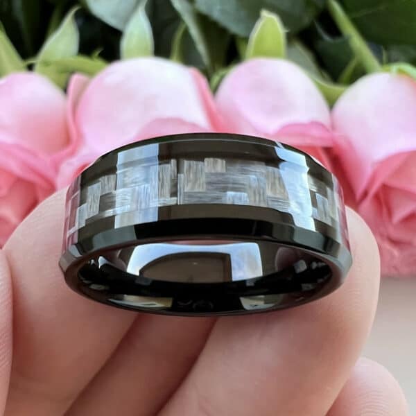 Three fingers carrying an 8mm black modern wedding band that features a polished finish over carbon fiber inlay and beveled edges.