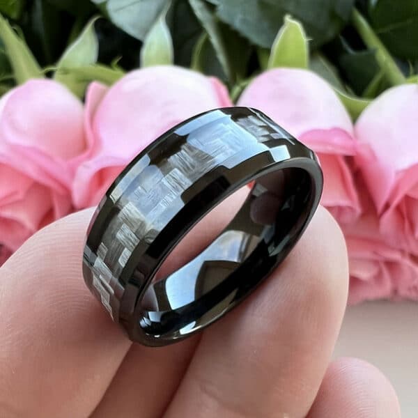 A 8mm contemporary men's wedding ring with a carbon fiber inlay, polished finish and sleeve, and beveled edges, balances on three fingers.