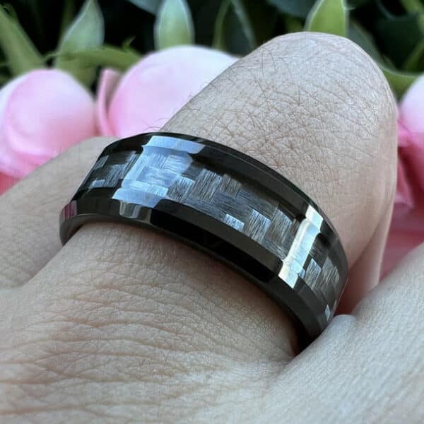 A ring finger with a contemporary comfort-fit wedding ring that features a carbon fiber inlay, unique design, polished finish, and beveled edges.