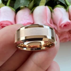 An 18K gold-plated modern wedding band with classic features like a brushed center and polished beveled edges resting on finger tips.
