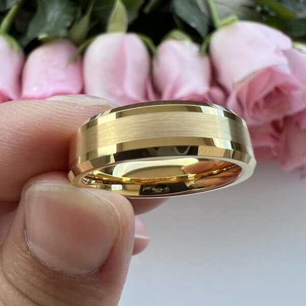 Three fingers holding an 18k gold-plated 6mm wedding ring for men, featuring a brushed center and polished beveled edges.