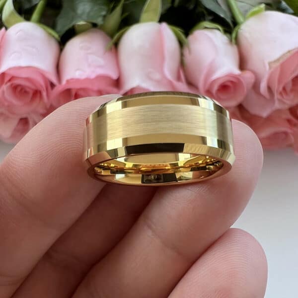 Three fingers hold up a 18k gold-plated men's tungsten wedding band and exposes its brushed finish and polished beveled edges.