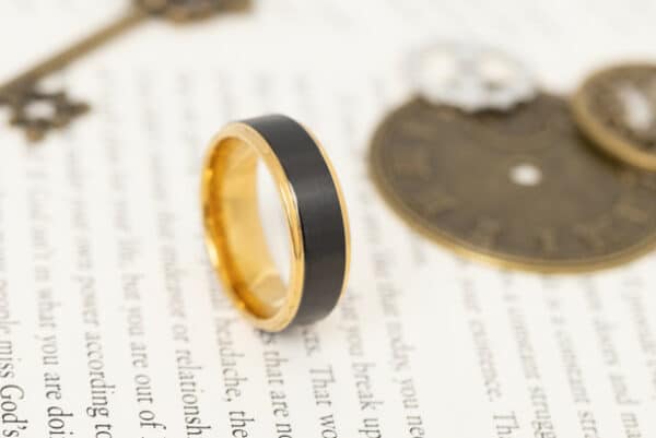 A black men's wedding band with gold brushed center, gold edges, and polished sleeves.