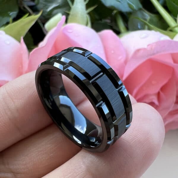 Side view of a black modern wedding ring with a brushed finish, polished edges and sleeve, and carved design.