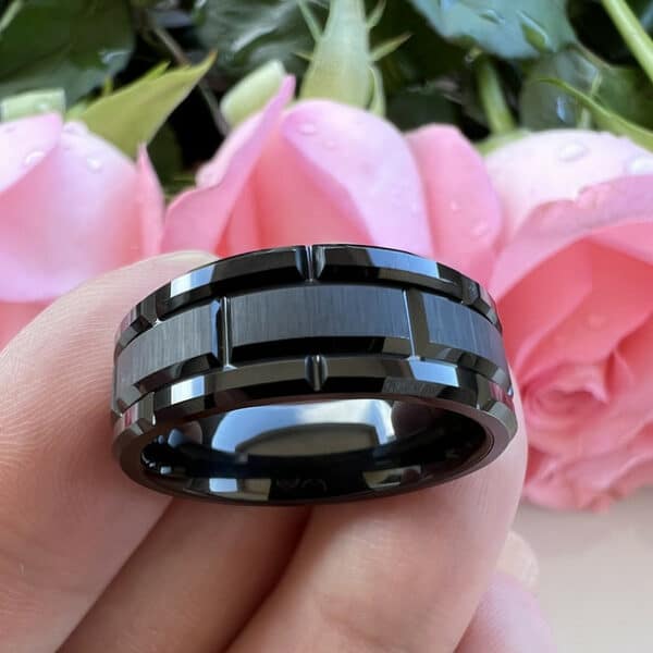 Black modern wedding band for men featuring a carved design, polished edges, and brushed center on a man's fingers.