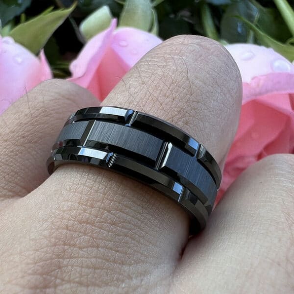 Black wedding ring for men with carved design, brushed center, and polished edges on a man's ring finger.