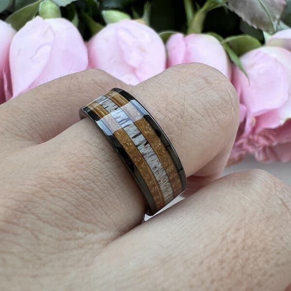 A ring finger wears the Payson to showcase its unique black edges, whiskey barrel oak sides, deer antler center, and 8mm width.