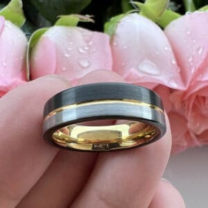 A black and silver brush finish men's wedding ring featuring a gold pinstripe and sleeve, resting on three fingers.