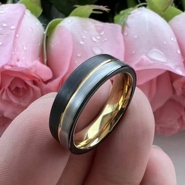 18K gold pinstripe separating a silver brushed end and a black brushed end of a modern men's wedding band, resting on three fingers.