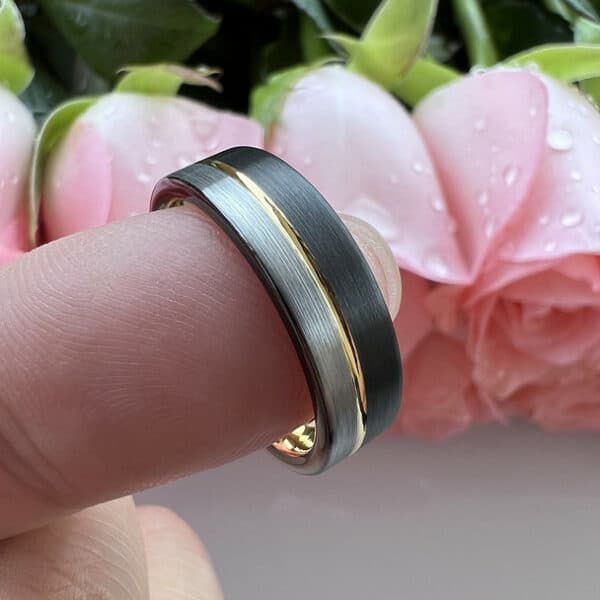A silver and black brush finished modern men's wedding ring with an 18K gold pinstripe through its middle, resting on the tip of a finger.