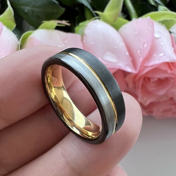Black and silver brushed ends wedding band for men with gold pinstripe and sleeve, resting on a man's fingers.