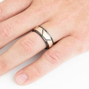 A ring finger with The Liam, showcasing its faceted rose gold plated inlay, black beveled edges, and sleeve with its polished finish.