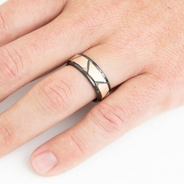 A ring finger with The Liam, showcasing its faceted rose gold plated inlay, black beveled edges, and sleeve with its polished finish.