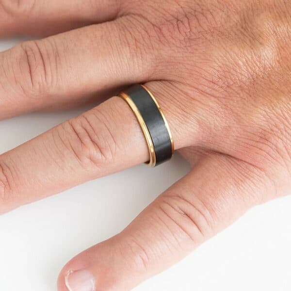An 8-mm gold-accented black wedding ring with a sleek design on a finger.