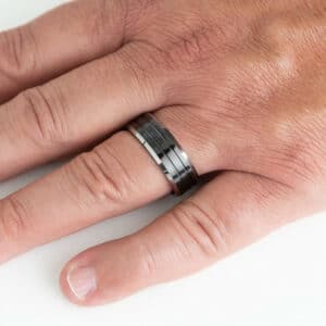 The Trevor men's wedding band on a ring finger showcasing its grooved center design, silver edges, and polished finish.