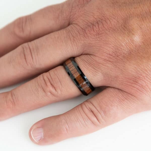 A hand with the ring finger wearing a black ring with embedded KOA wood.