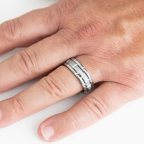 A spread-out hand displaying an 8mm wedding ring featuring a carved pattern design, brushed center, and polished beveled edges.