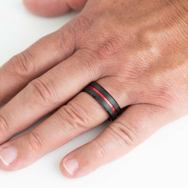 A hand wearing an 8mm tungsten black wedding ring with red grooves and sleeves.