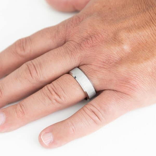 A minimalist men's wedding ring on a finger, featuring a satin finish and polished edges that extend to its sleeve.