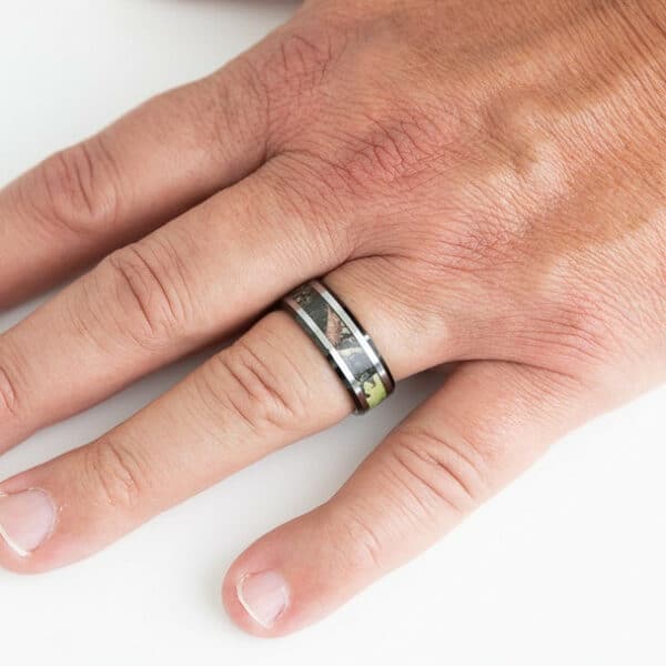 The James on a ring finger showing its silver and black edges, camo inlay, and polished finish.