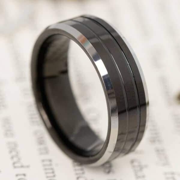 The Trevor, a black men's tungsten wedding ring shows its grooved center design, silver polished edges, and dark sleeve.