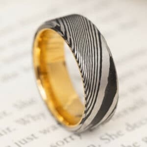 An 8mm Damascus steel wedding ring with yellow gold stainless steel sleeves.