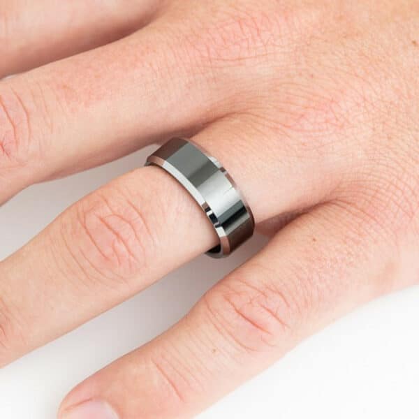 A black men's wedding band, The Price, with its polished finish and silver edges, creating a striking contrast.