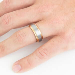 A man’s hand wearing a tungsten carbide ring with plated gold edges and brushed finishes.