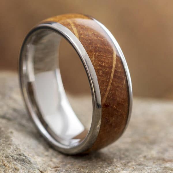 A minimalist and nature-inspired men's band with a whiskey barrel oak wood inlay, domed design, crisscross pattern, and silver polished edges and sleeves.
